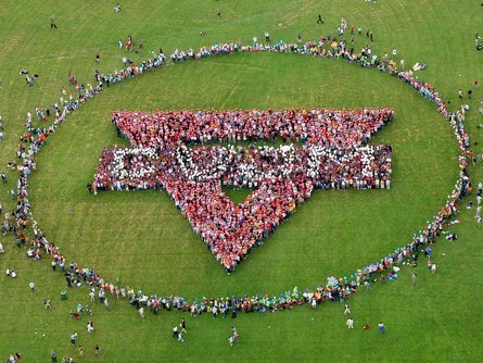 Menschen bilden riesigen Kreis mit CVJM Logo auf grüner Wiese